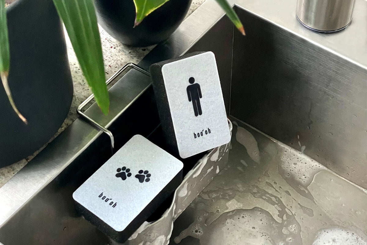 Paw-print and person-labeled Mogo sponges resting beside a stainless-steel kitchen sink, keeping pet-dish and household cleaning tools visually separated.