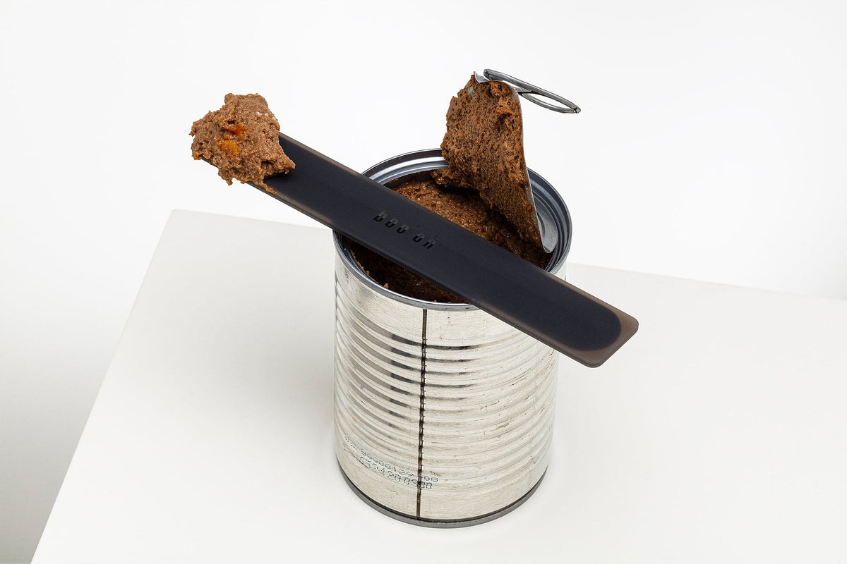 Black Mogo Spatula balanced across an open pet-food can with portions of wet food resting on the utensil.
