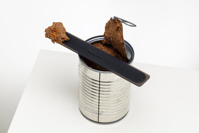 Black Mogo Spatula balanced across an open pet-food can with portions of wet food resting on the utensil.