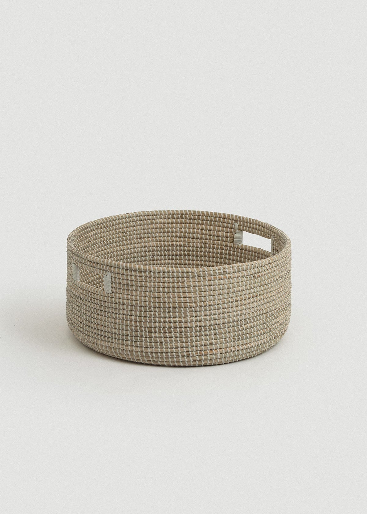 Low round seagrass floor basket with tightly woven natural fibers and two rectangular cutout handles.