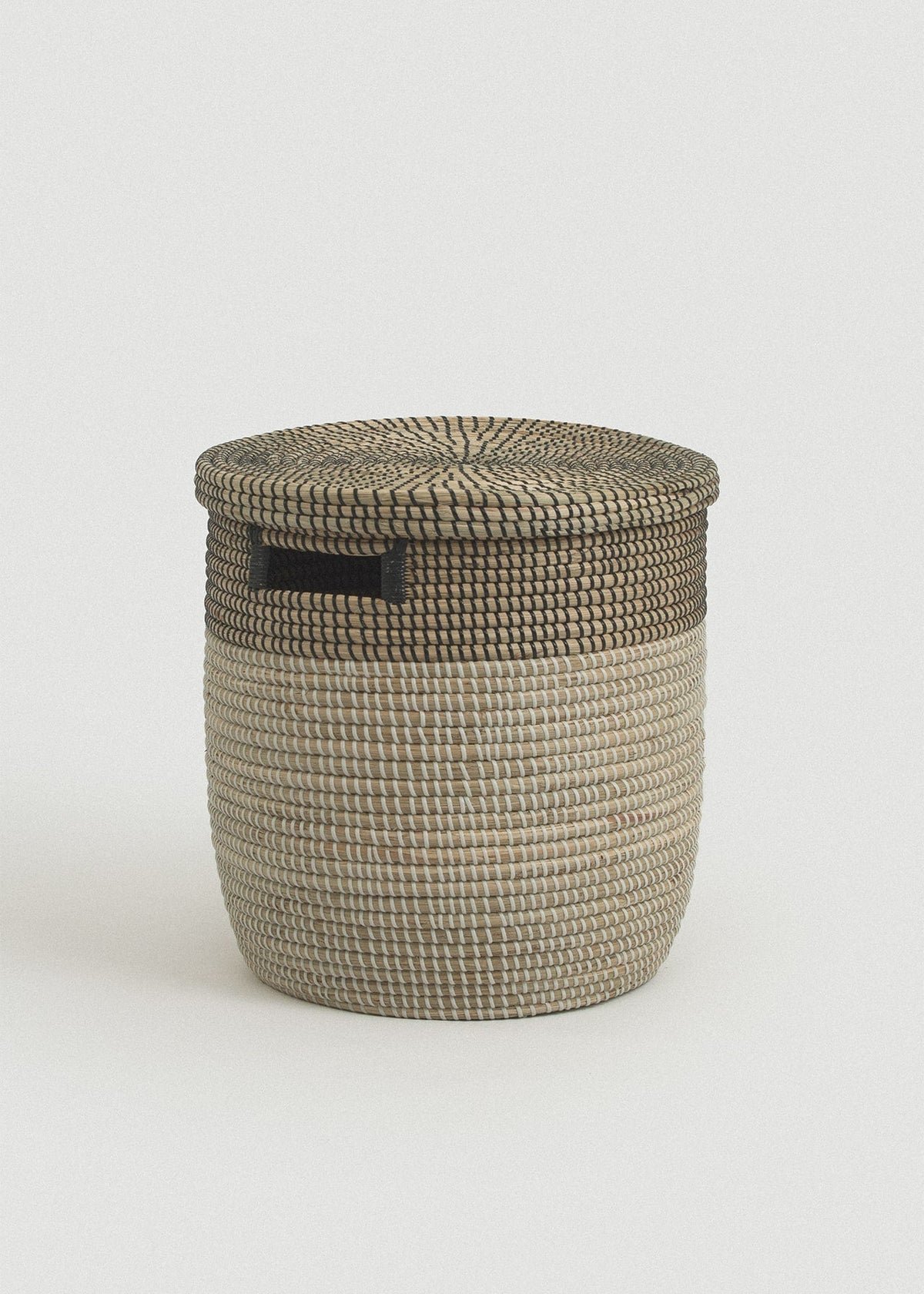 Two-tone woven seagrass storage basket with a natural body, black upper band, flat lid, and rectangular black handle.