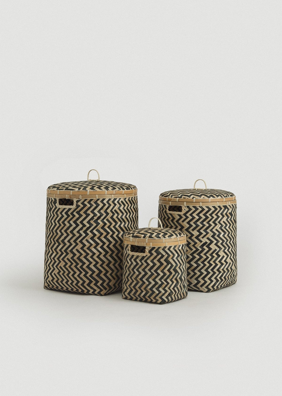 Set of three lidded bamboo storage baskets in graduated sizes with natural and black zigzag weaving.