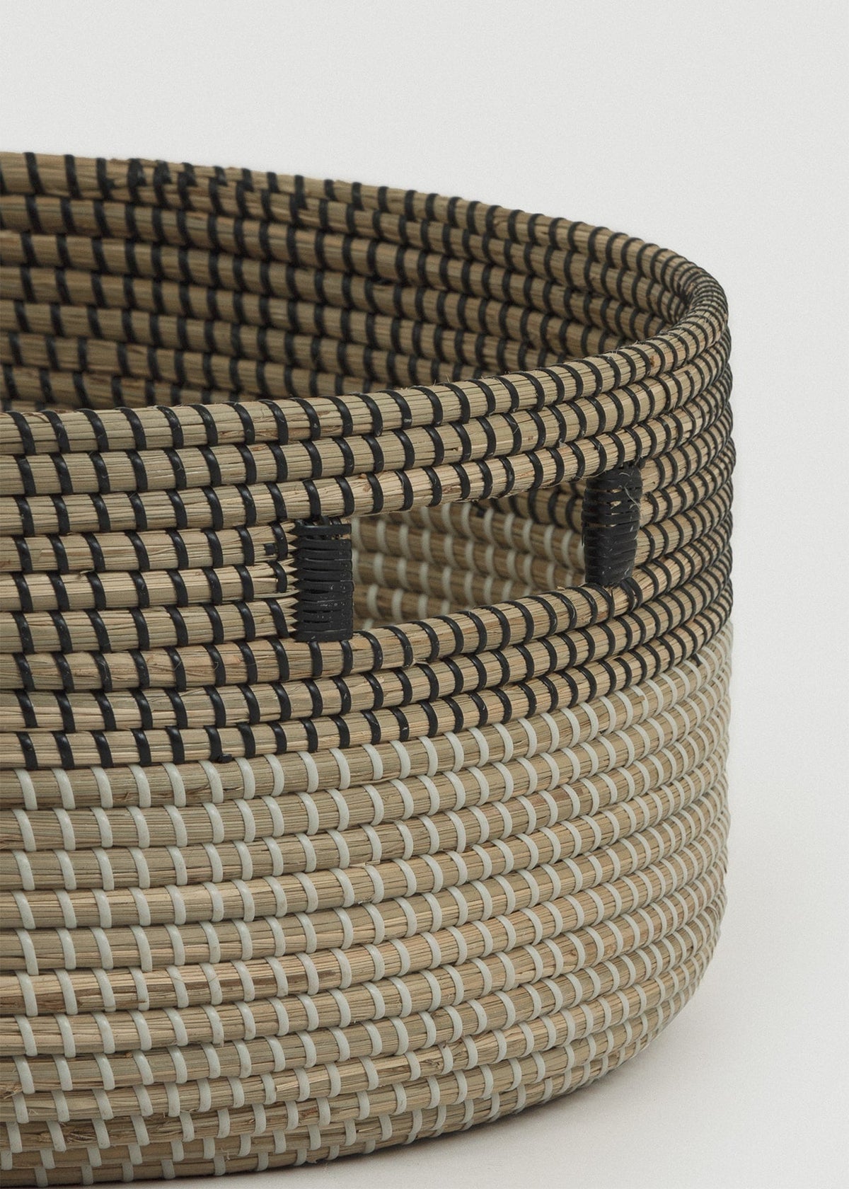 Close-up of the two-tone seagrass weave, dark upper band, thick rounded edge, and handle.