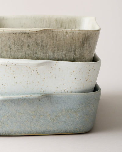 Close-up of three stacked Fieldstone Bakers in warm stone, speckled white, and blue-gray glazes, highlighting their handmade texture and softly uneven rims.