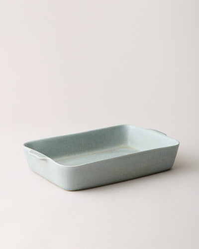 Empty blue-gray Fieldstone Baker shown alone from a low three-quarter angle, highlighting its shallow depth and softly curved rectangular shape.