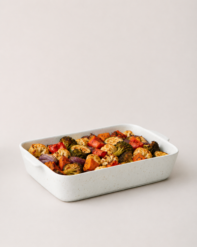 Speckled white Fieldstone Baker filled with roasted vegetables in red, green, orange, and golden-brown tones.