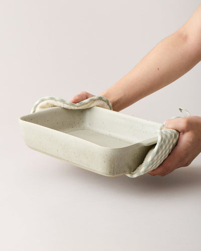 Hands protected by thick oven mitts holding an empty warm stone Fieldstone Baker, demonstrating its size and side grips.
