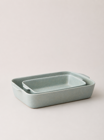 Two blue-gray Fieldstone Bakers nested together, showing their smooth pale glaze, rounded corners, and integrated handles.