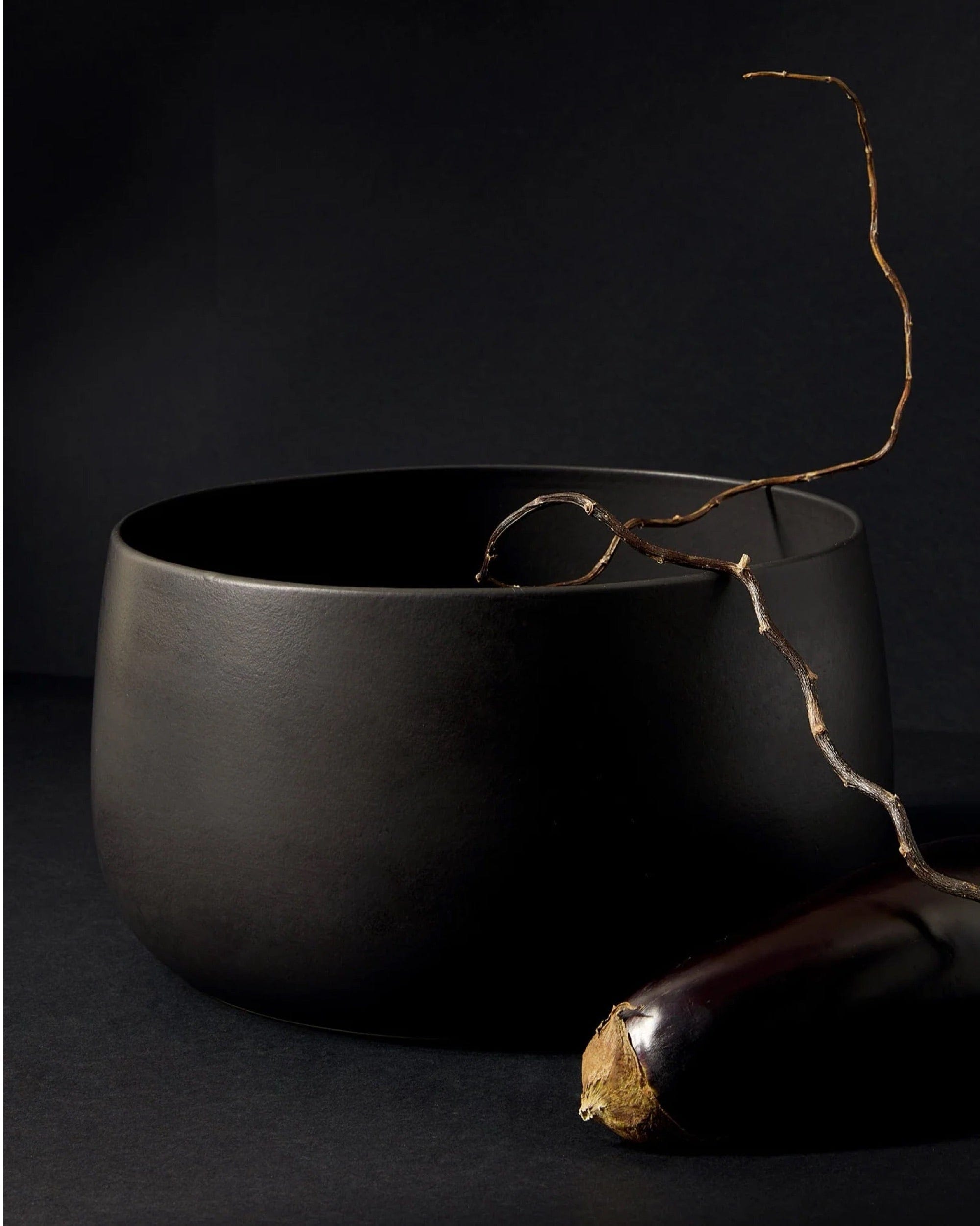Stoneware serving bowl 120 oz in Matte Black styled with dried branch and eggplant