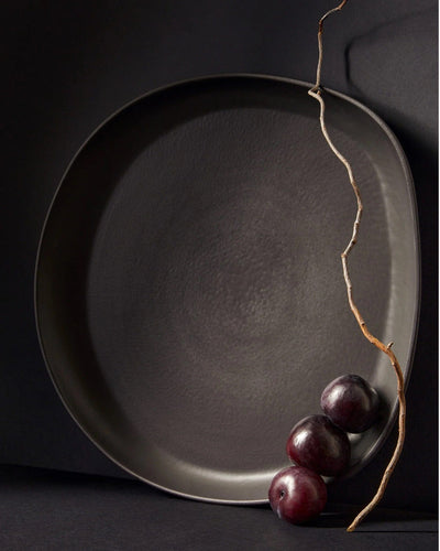 Stoneware round serving platter in Matte Black holding fresh plums