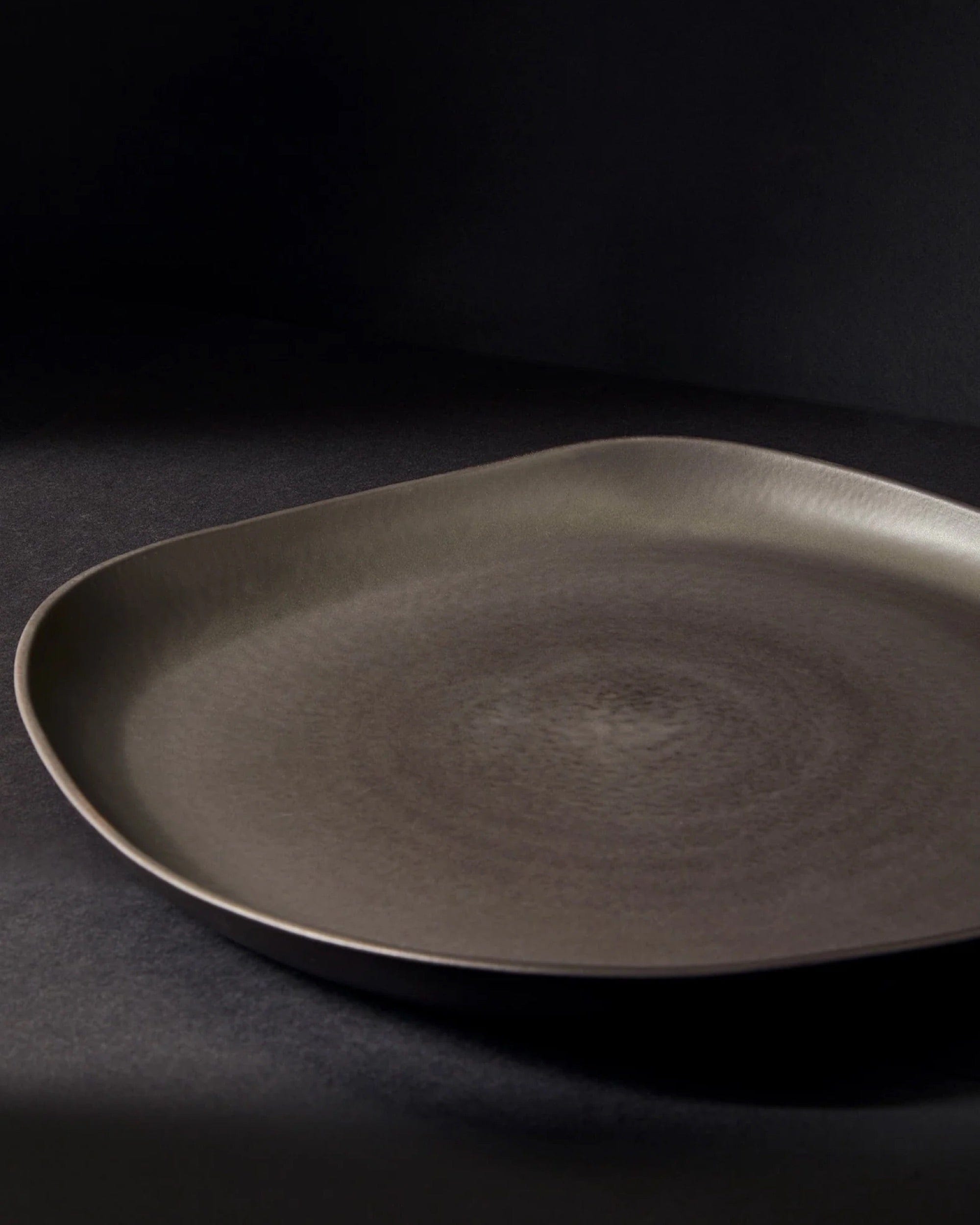 Stoneware round serving platter in Matte Black angled view on dark background