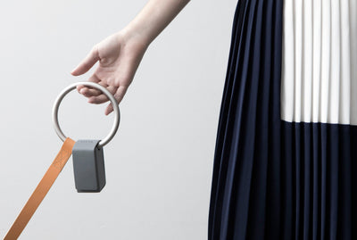 Hand holding the leash’s oversized silver ring handle with a small black waste-bag holder attached, while the peach strap extends downward.