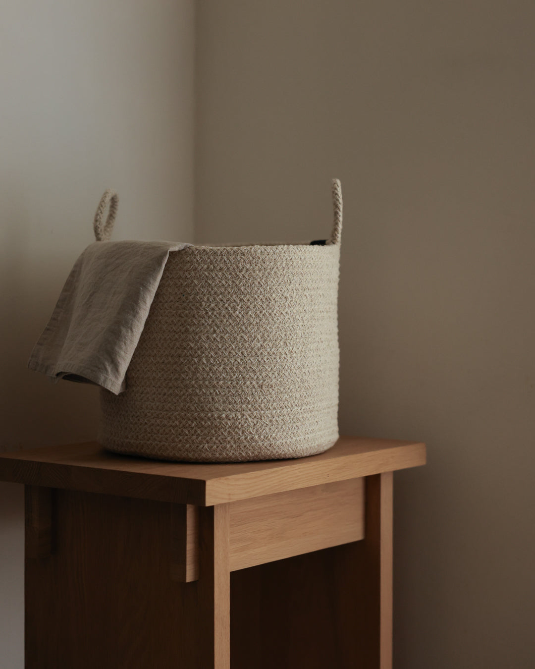 Beige Melange Loops basket on a wooden table with a gray cloth draped over the rim.
