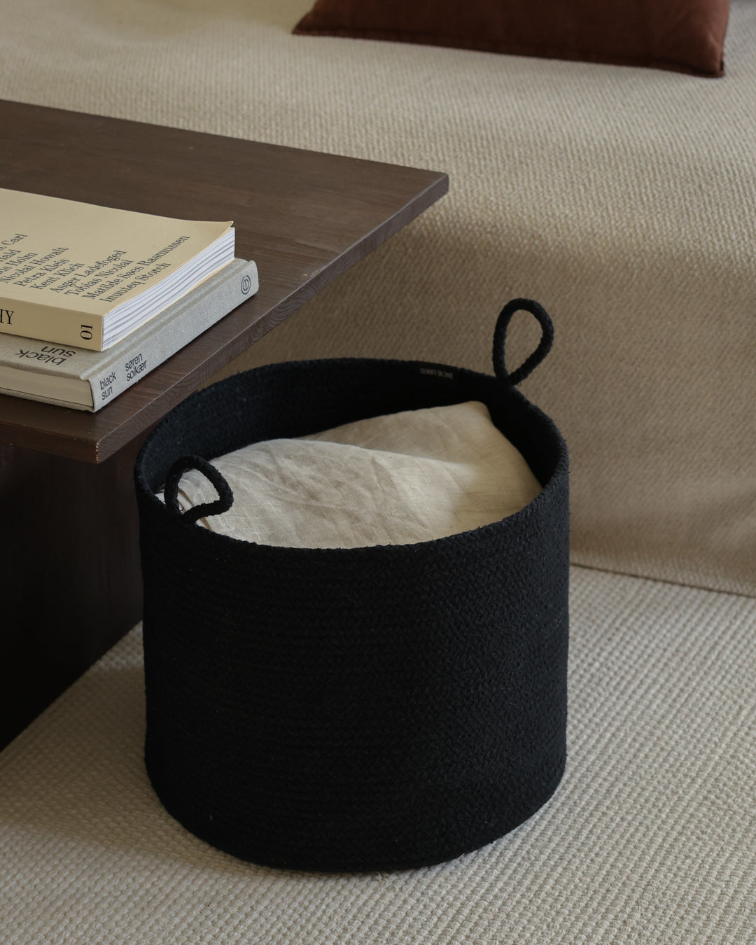 Black cotton basket filled with a folded blanket beneath a dark wood side table.