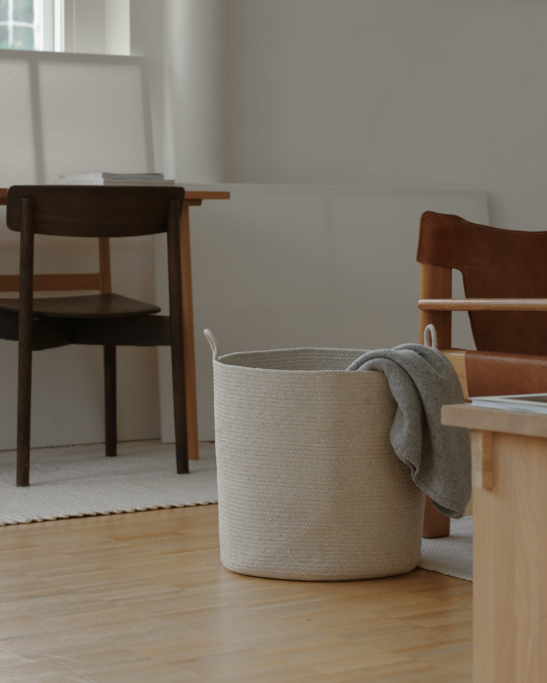 Beige rope basket with a gray throw draped over the rim in a softly lit living space.