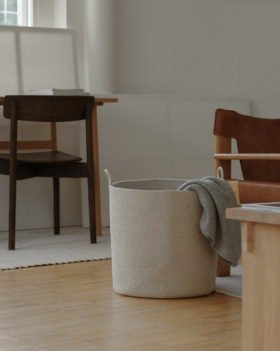 Beige rope basket with a gray throw draped over the rim in a softly lit living space.