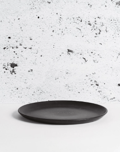 Stoneware dinner plate in Matte Black side profile view against textured concrete background