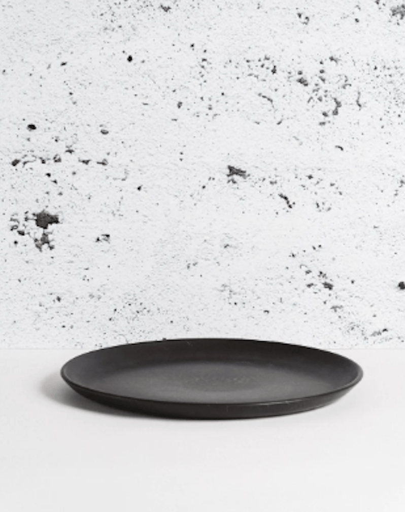 Stoneware dinner plate in Matte Black side profile view against textured concrete background