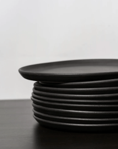 Stoneware dinner plates in Matte Black stacked on dark wood surface