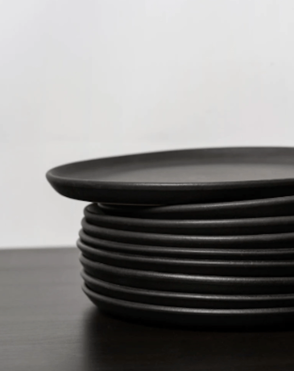 Stoneware dinner plates in Matte Black stacked on dark wood surface