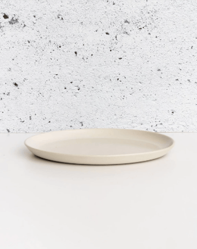 Stoneware dinner plate in Matte White side profile view against textured concrete background