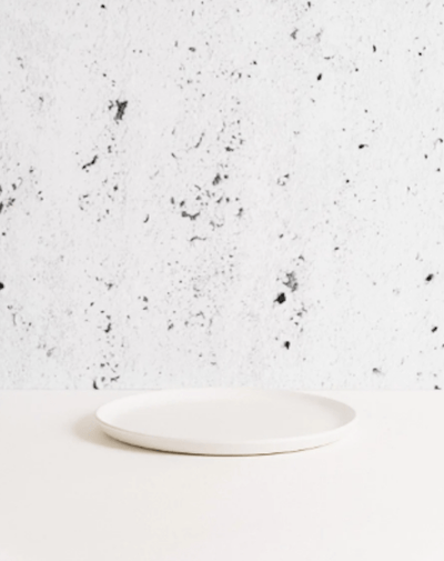 Stoneware side plate in Matte White side profile view against textured concrete background