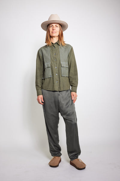 Front view of a model wearing the olive Trek Shirt with loose gray pants and a beige hat.