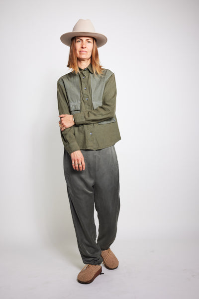 Model posing with crossed legs in charcoal Souk pants and an olive jacket.