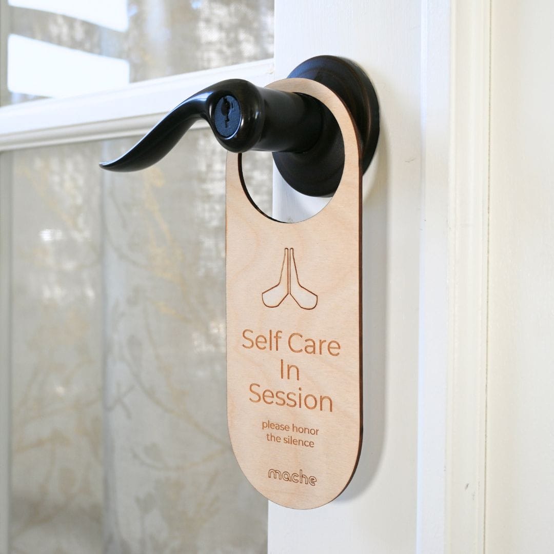 Light natural wood version of the self-care door hanger, engraved with the same meditation symbol, quiet-time message, and small Mache logo.