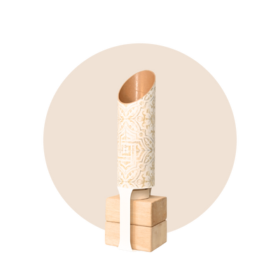 Cream-and-gold patterned cylindrical yoga mat holder standing upright on a four-block natural wood base, framed by a pale beige circle.