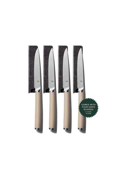 Set of four knives with beige handles and black blade guards on a green background.