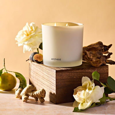 APOTHEKE Cedarwood Ginger 3-Wick Candle styled on a wood block with white flowers, figs, and fresh ginger root