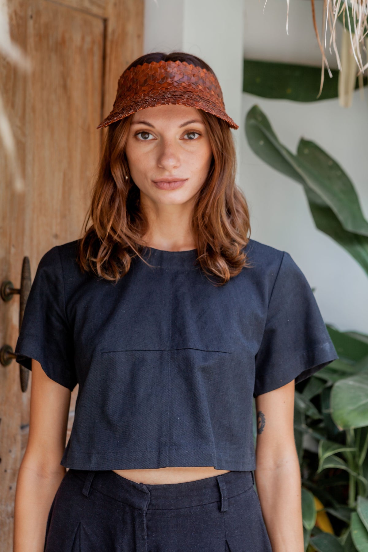 Village Thrive Rattan Sun Visor, clay palm leaf, worn by a model standing.