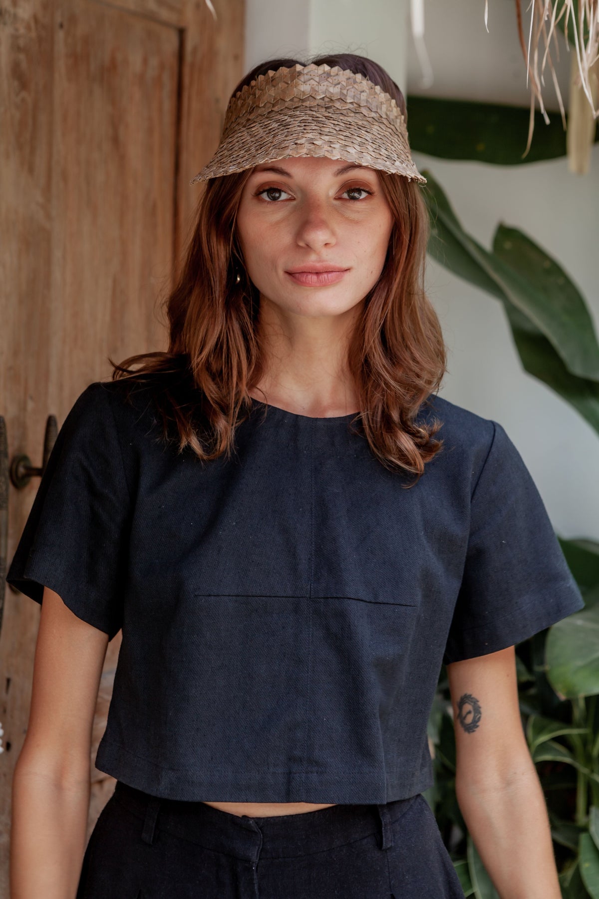 Village Thrive Rattan Sun Visor, blonde palm leaf, worn by a model standing.