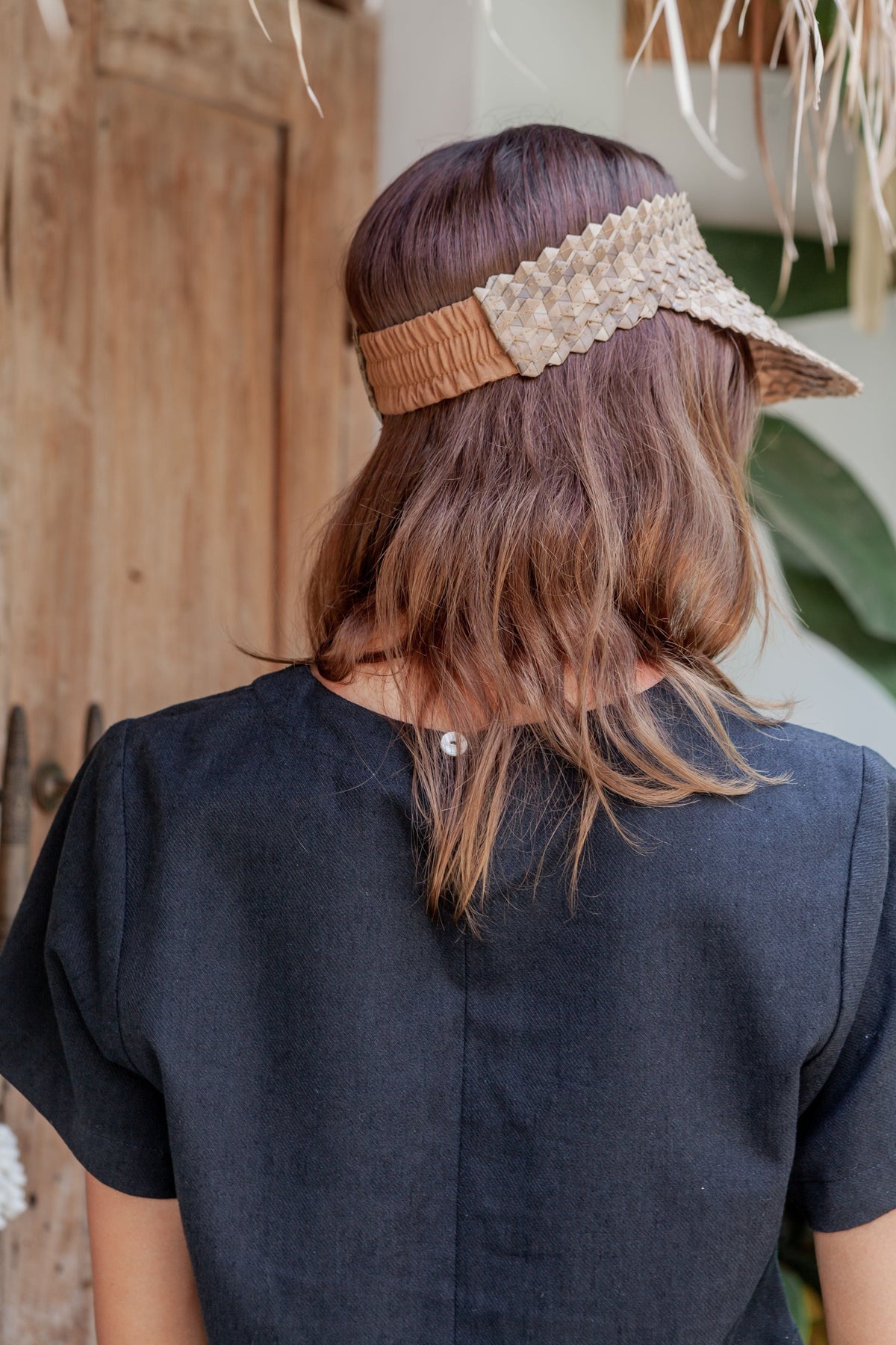Village Thrive Rattan Sun Visor, blonde palm leaf, worn by a model from behind.