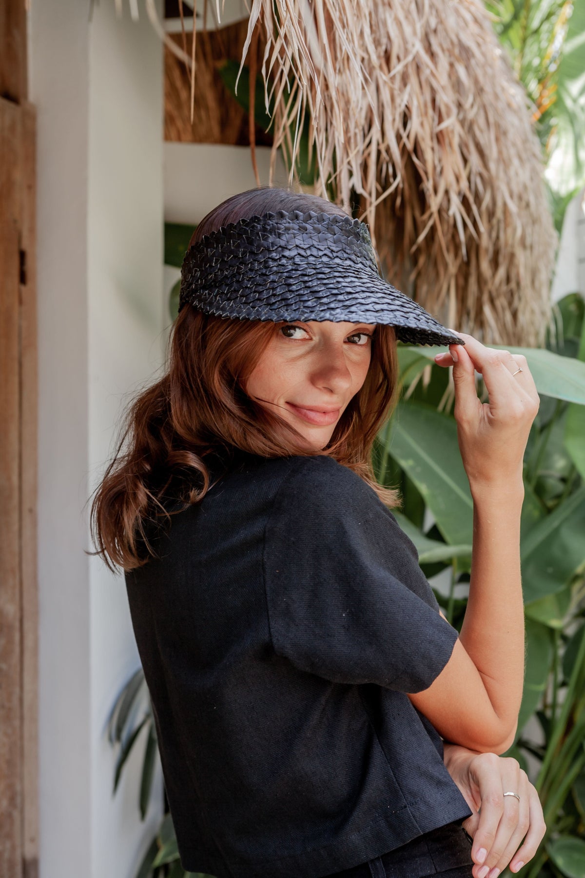 Village Thrive Rattan Sun Visor, black palm leaf, worn by a model adjusting the visor.