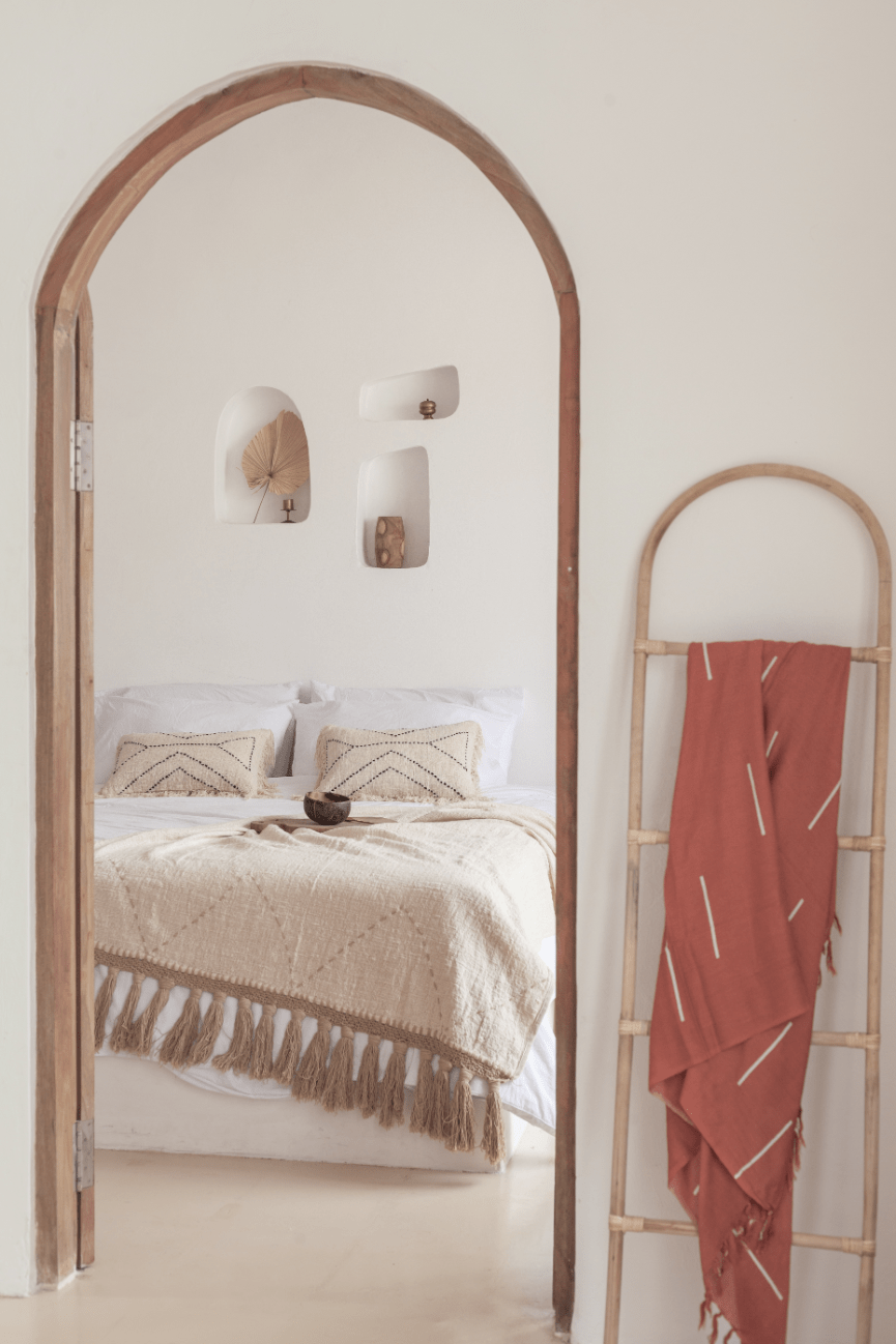 Village Thrive Lines Tapestry, terracotta rayon, draped over a wooden ladder beside an arched mirror in a bedroom.