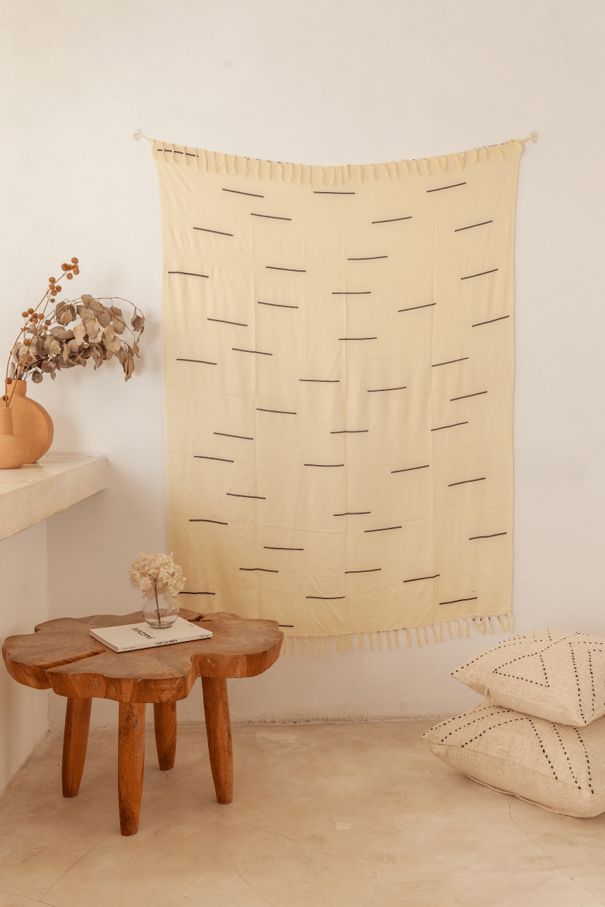 Village Thrive Lines Tapestry, mustard yellow rayon with white line print, hanging above a wooden stool and floor cushions.
