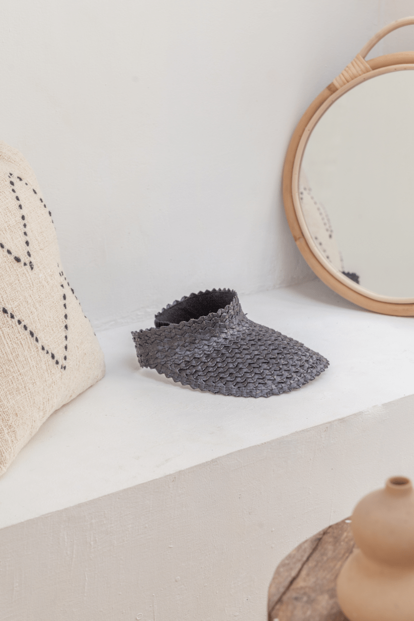 Village Thrive Rattan Sun Visor, black palm leaf, displayed on a shelf beside a round mirror.