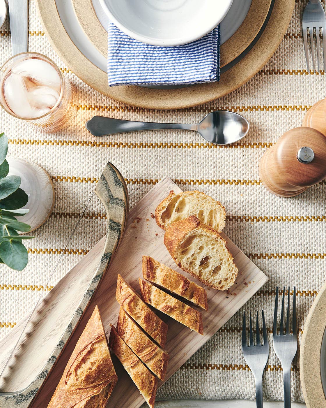 Bread bow and diagonally sliced baguette styled on a cutting board within a layered neutral table setting.