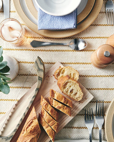 Bread bow and diagonally sliced baguette styled on a cutting board within a layered neutral table setting.