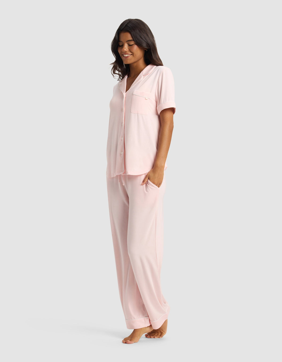 Side view of the pale pink pajama set, showing the relaxed drape of the short-sleeve top and straight-leg pants, with one hand in a pants pocket.