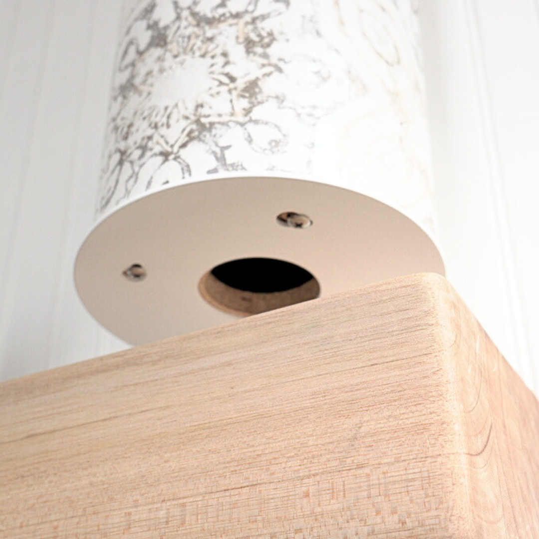 Low-angle detail of the pale wood base’s underside, showing a round opening and metal fasteners.