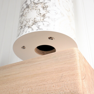Low-angle detail of the pale wood base’s underside, showing a round opening and metal fasteners.