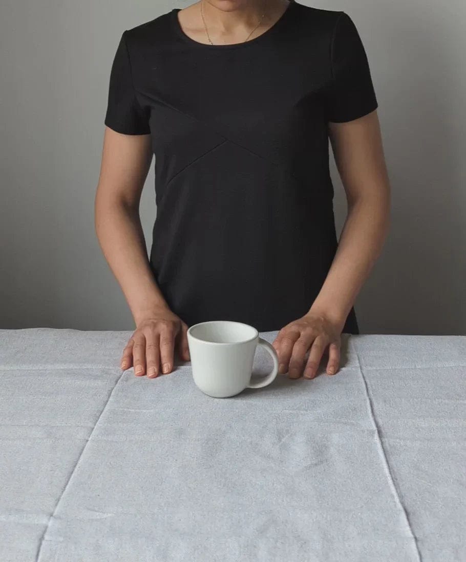 Person placing stoneware mug in Matte White on linen tablecloth to show scale