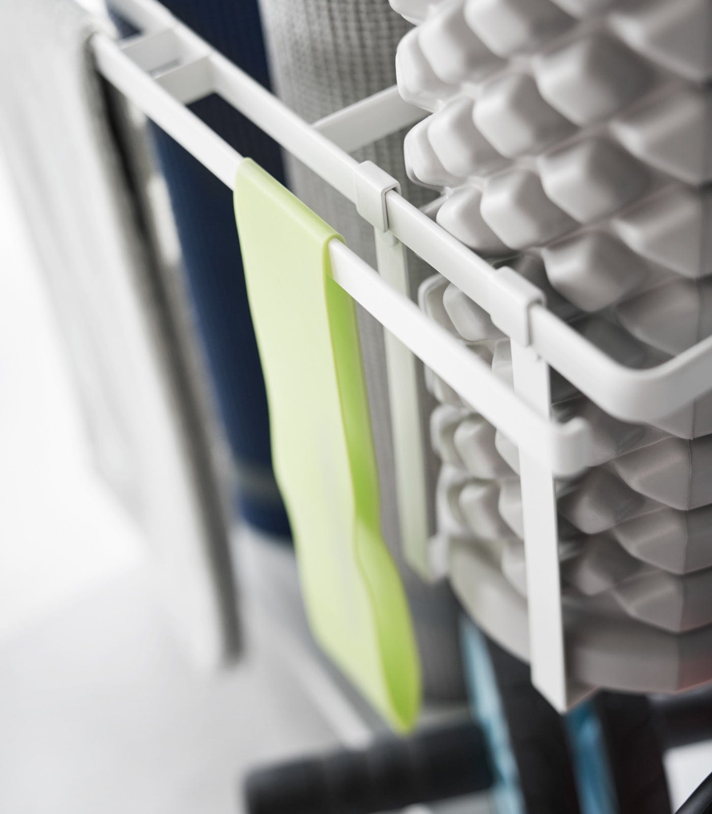 Stack of foam rollers and a green brush on a white rack.