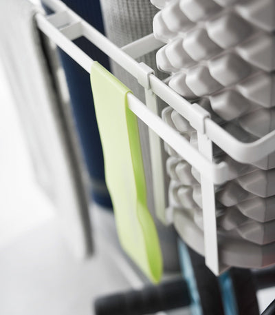 Stack of foam rollers and a green brush on a white rack.
