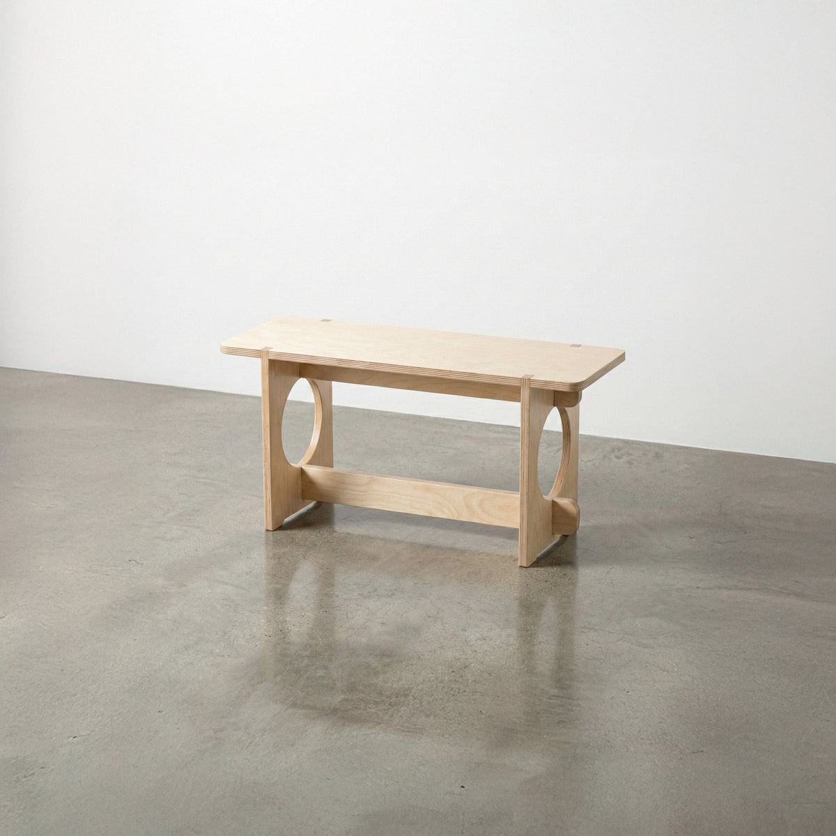 Studio Furnis YOYO natural wood bench with a rectangular seat, rounded corners, circular side openings and a low support rail on a polished concrete floor