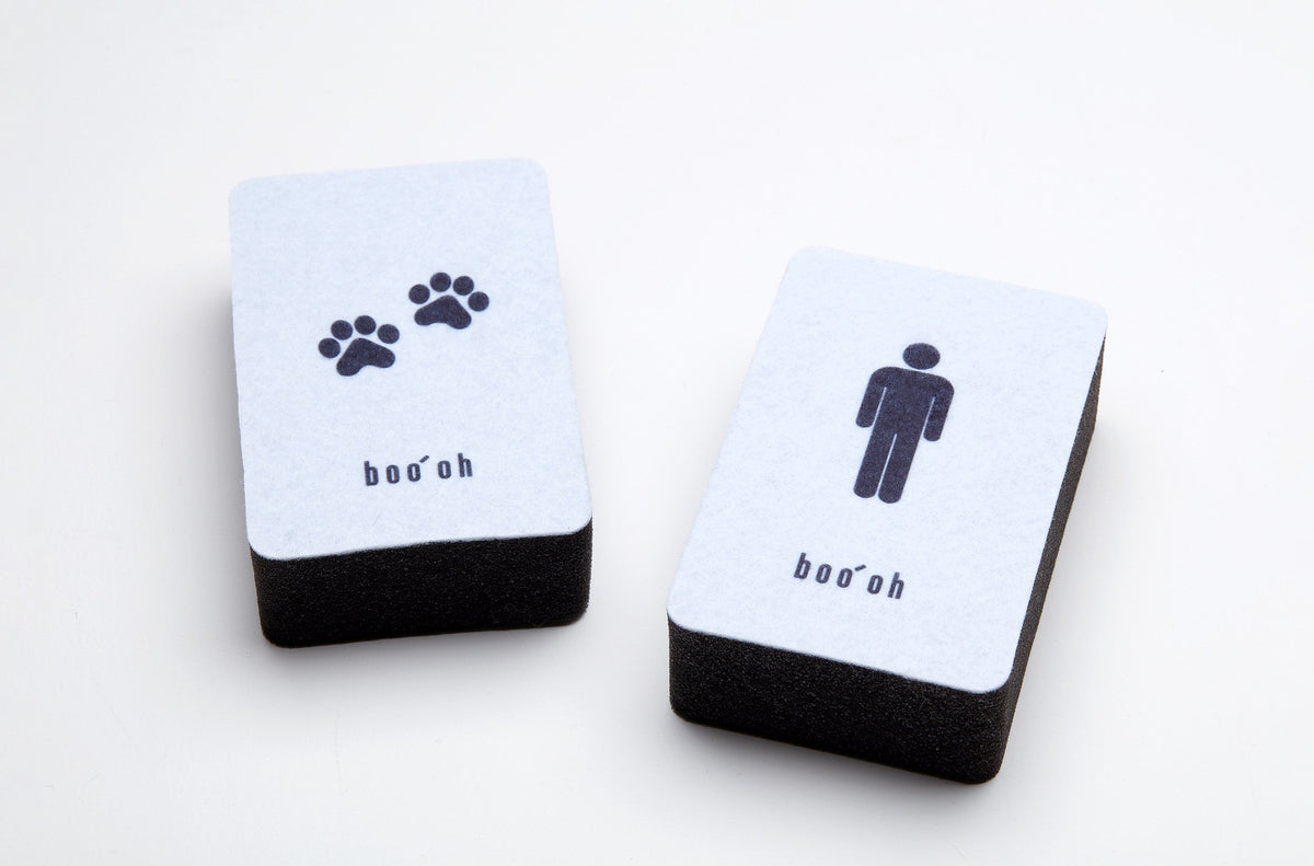 Two rectangular dual-layer cleaning sponges with white scrub surfaces and thick black foam bases; one is marked with paw prints and the other with a person icon.