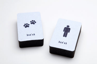 Two rectangular dual-layer cleaning sponges with white scrub surfaces and thick black foam bases; one is marked with paw prints and the other with a person icon.